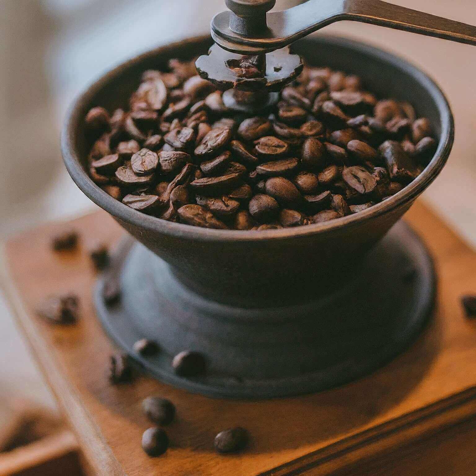 Vintage coffee grinder filled with coffee beans on a wooden surface.