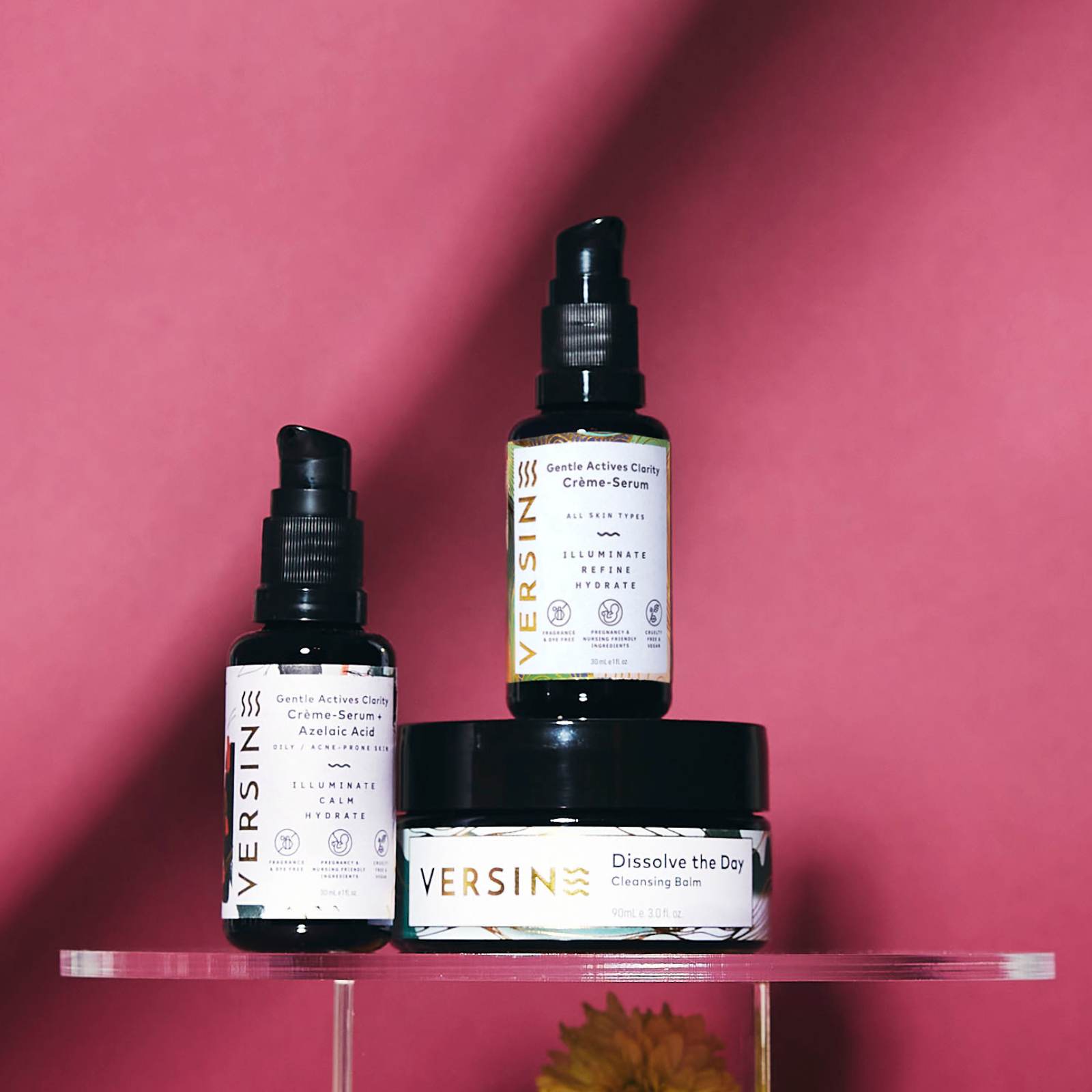 Three Versine skincare products on a clear stand against a pink background
