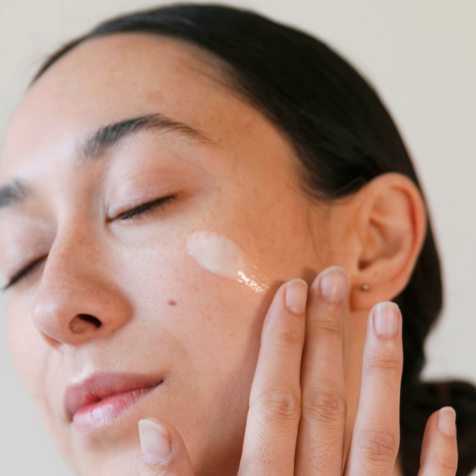 Woman applying cream to her face with a neutral background