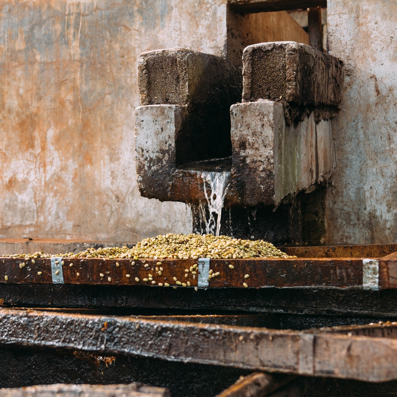 Old stone millstone grinding grain with water flowing, set against a rustic wall.