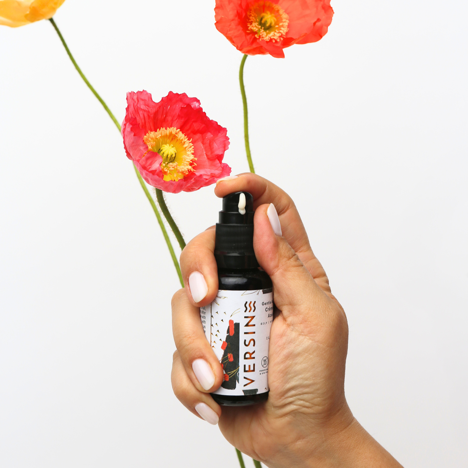 Hand holding a bottle labeled 'VERSIN' with red flowers in the background