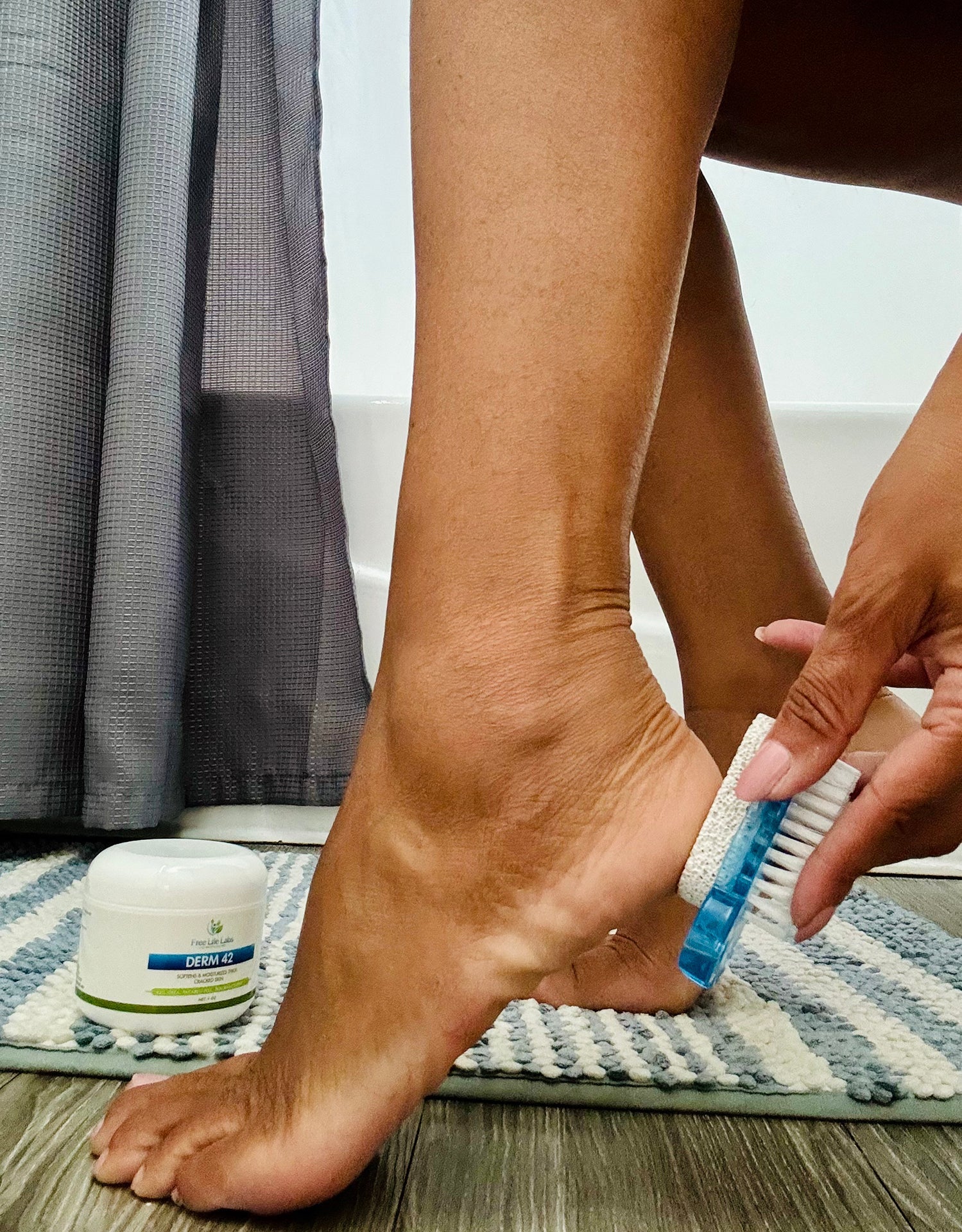 Person scrubbing their foot with a brush next to a jar of cream on a rug.