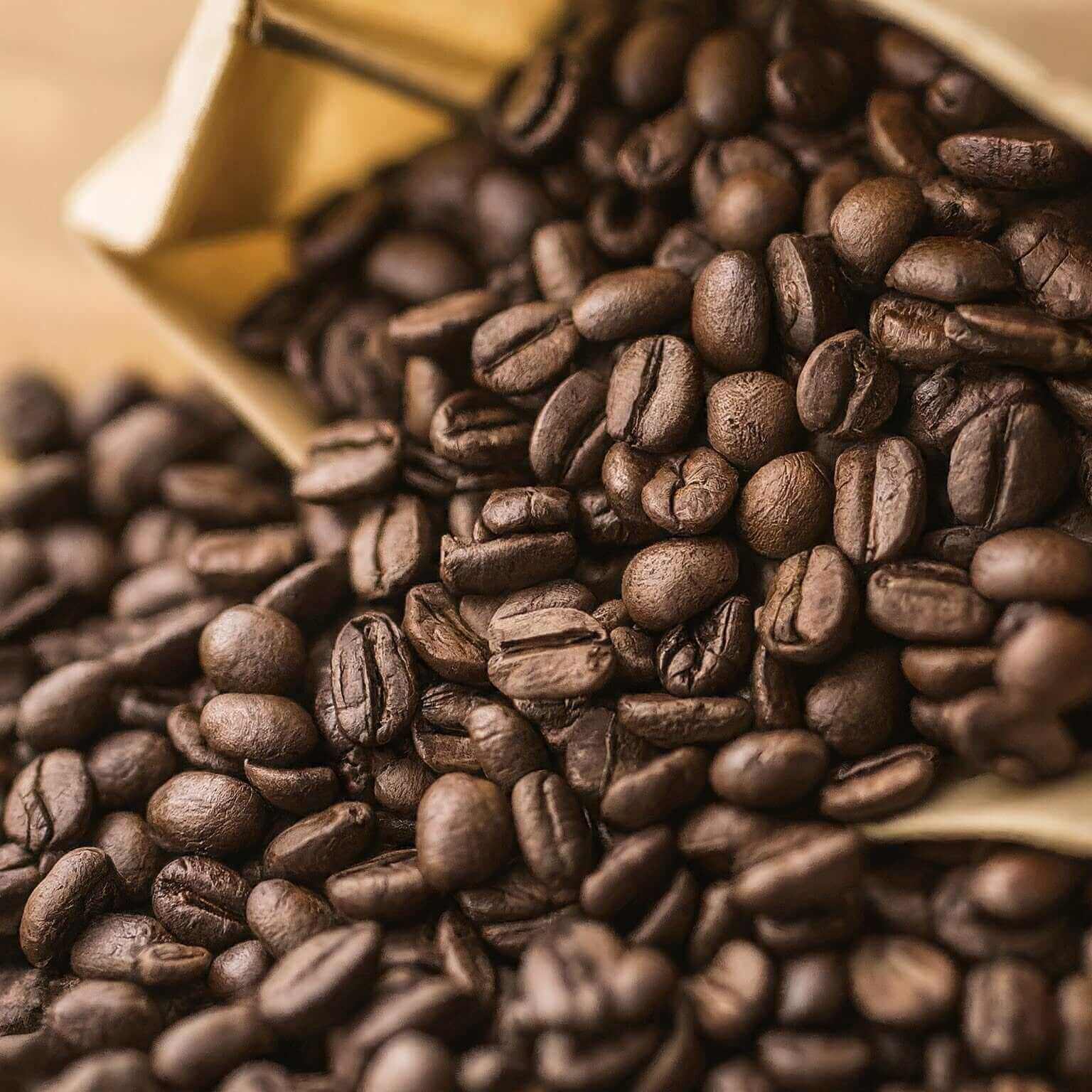 Close-up of roasted coffee beans with a gold container in the background