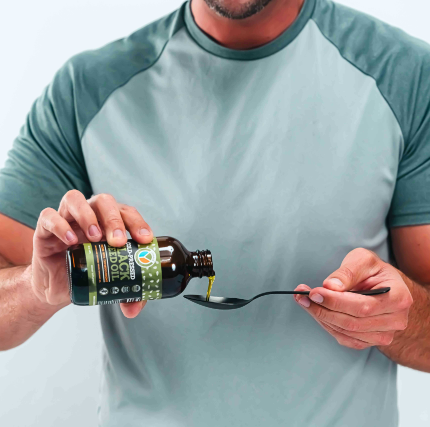 Person pouring oil from a bottle labeled 'Black Seed Oil' onto a spoon.