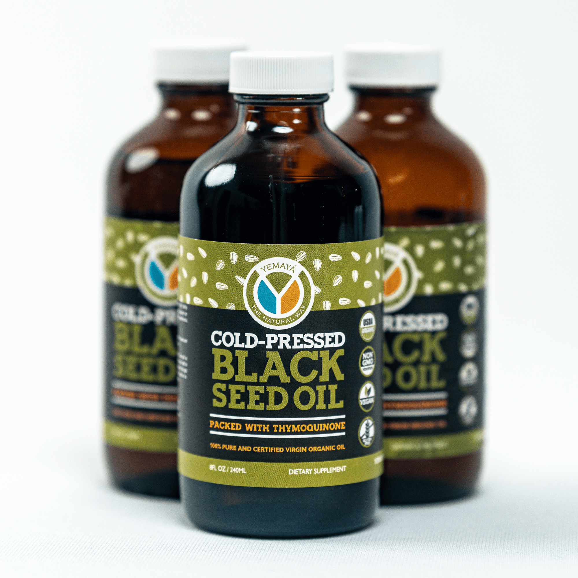 Three bottles of cold-pressed black seed oil with labels on a white background