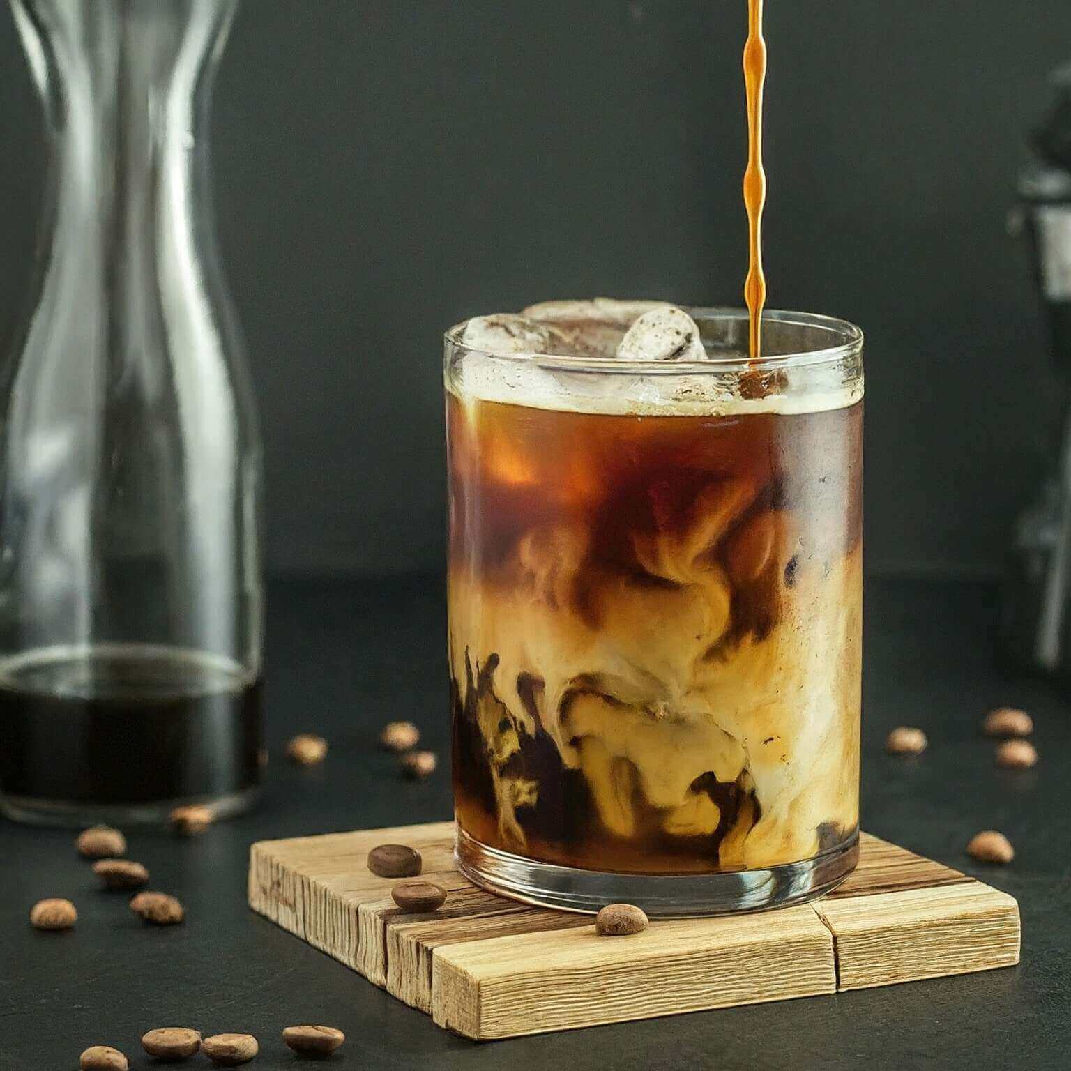 Glass of iced coffee with a pour, surrounded by coffee beans on a dark background