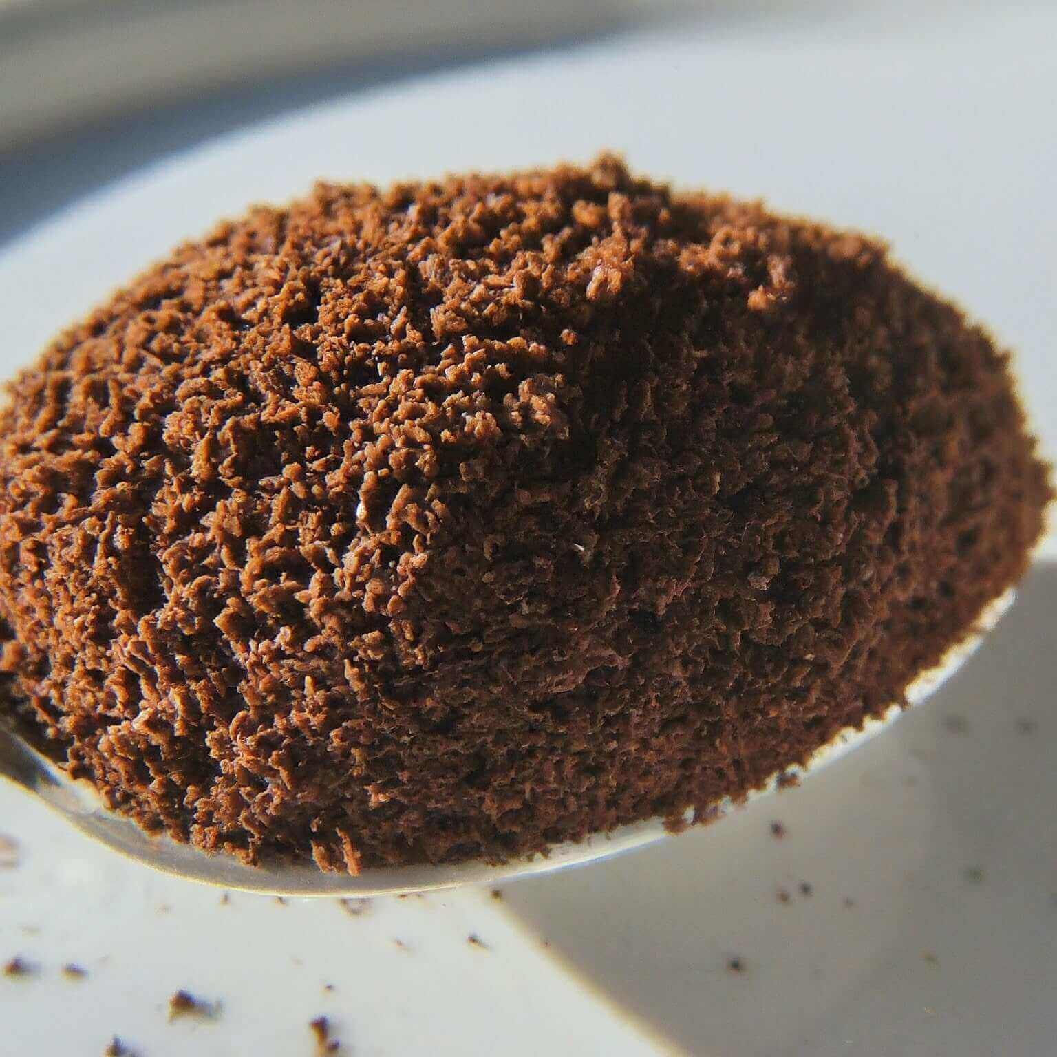 Close-up of a spoonful of dark brown coffee grounds on a white plate.