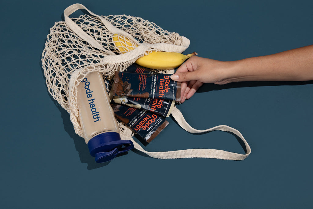 Hand holding a reusable mesh bag filled with groceries against a dark background