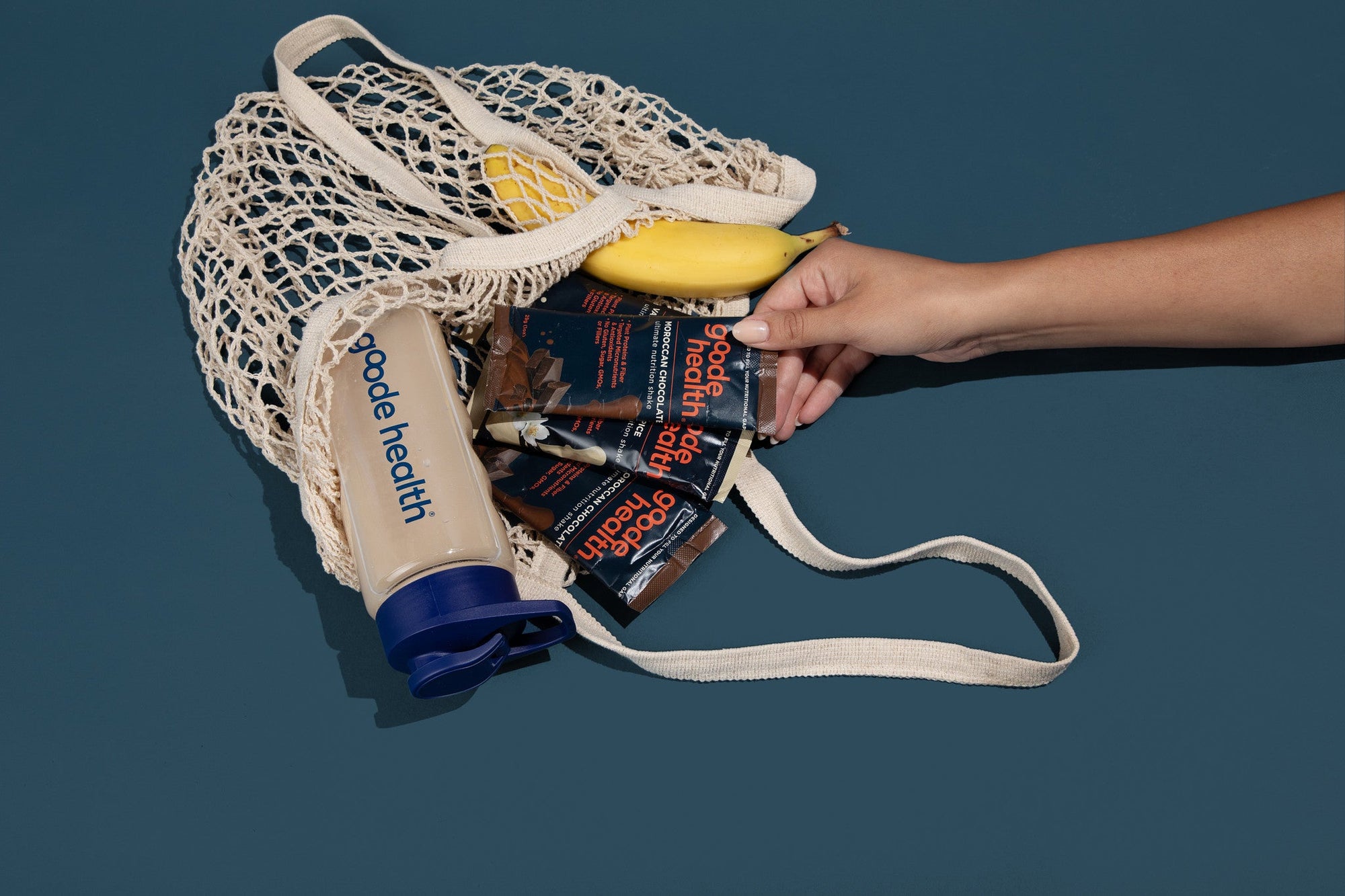 Hand holding a reusable mesh bag filled with groceries against a dark background