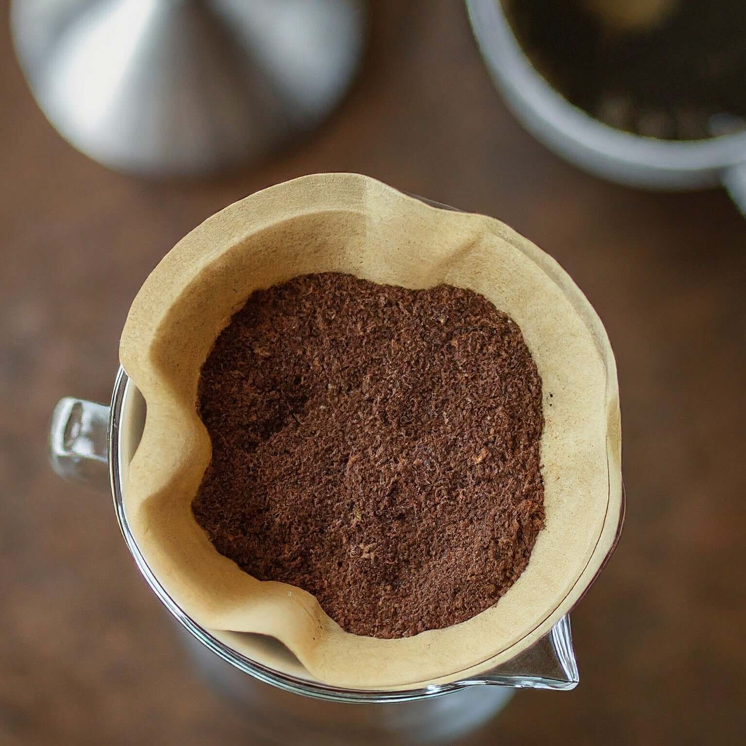 Coffee grounds in a brown filter on a clear glass mug with a blurred background