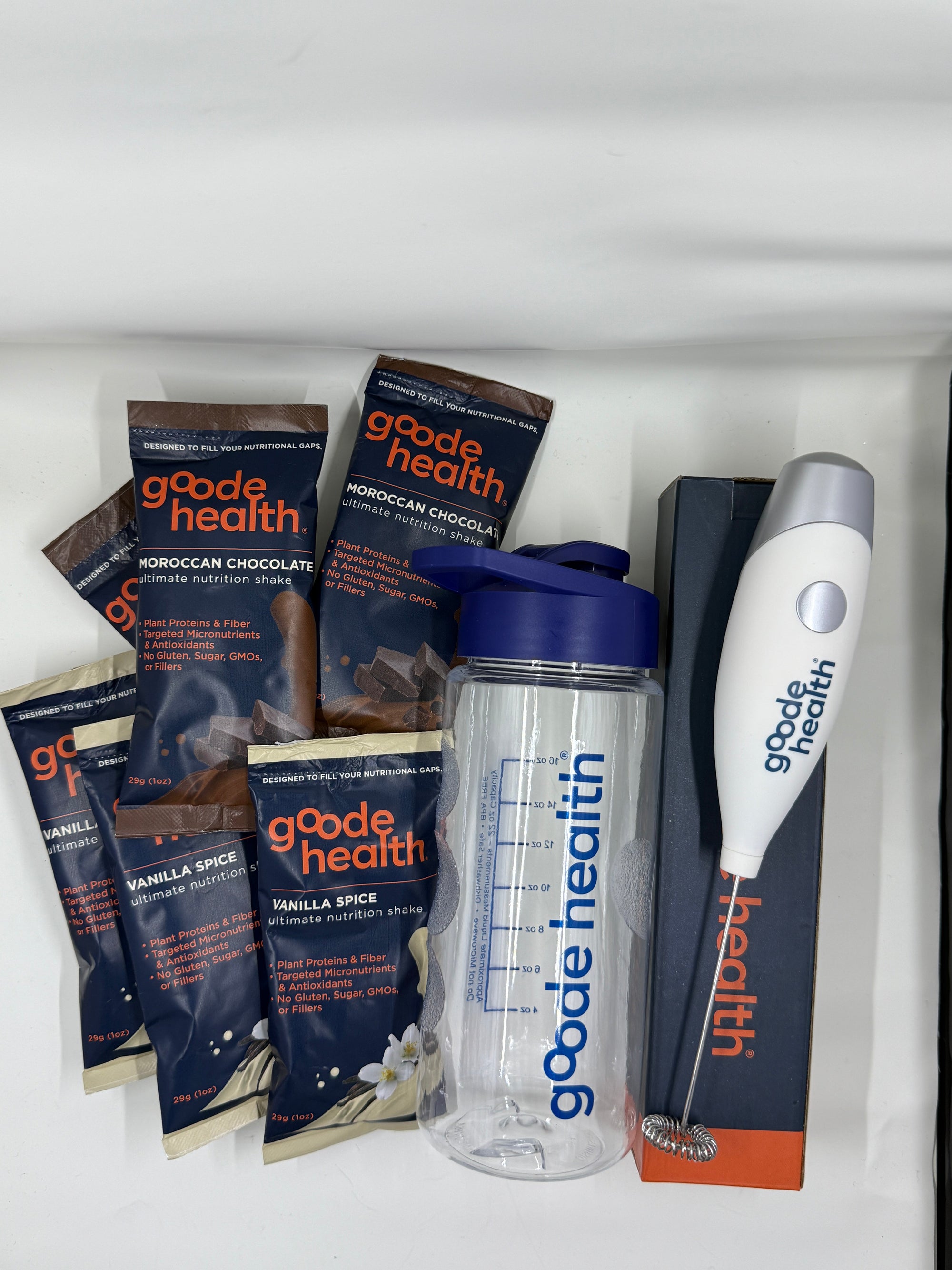 Collection of goode health products including packets, a tumbler, and a whisk on a white background.