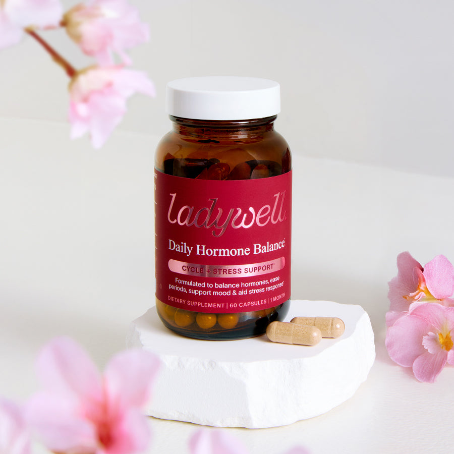 Bottle of Ladywell Daily Hormone Balance supplement with pink flowers in the background