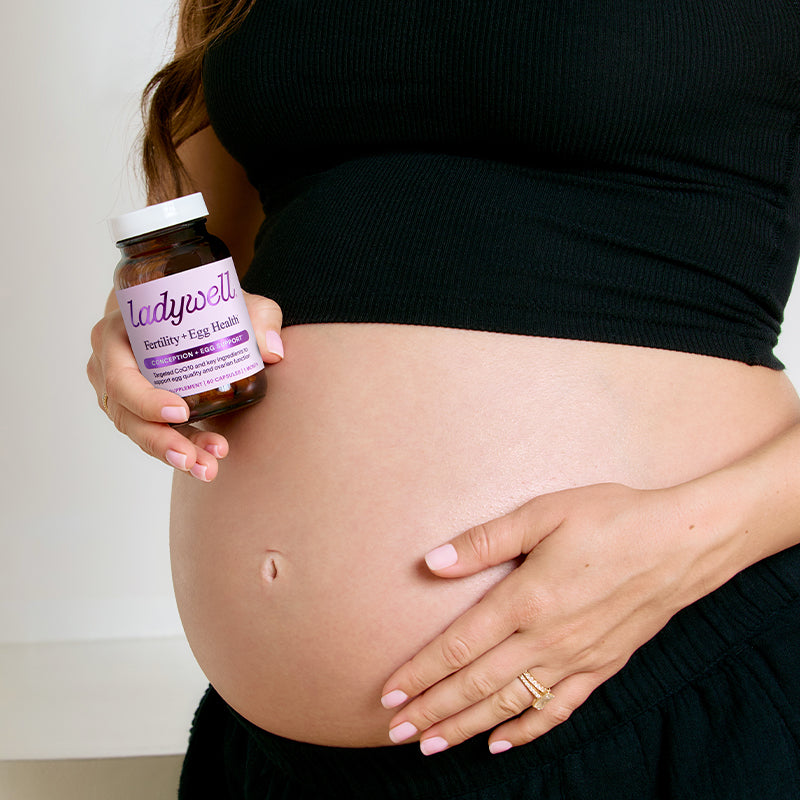 Pregnant person holding a bottle labeled 'ladywell' against a neutral background