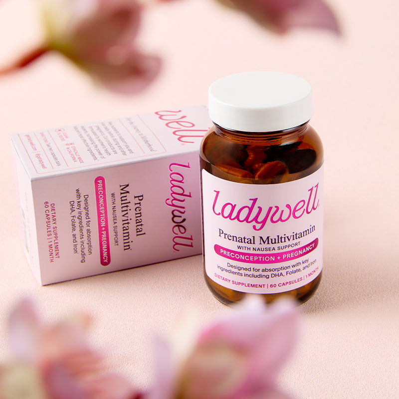 Bottle and box of Ladywell Prenatal Multivitamin on a light pink background with blurred flowers.