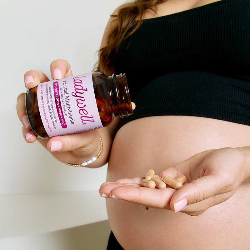 Pregnant woman holding a bottle of Ladywell prenatal multivitamin and pills.