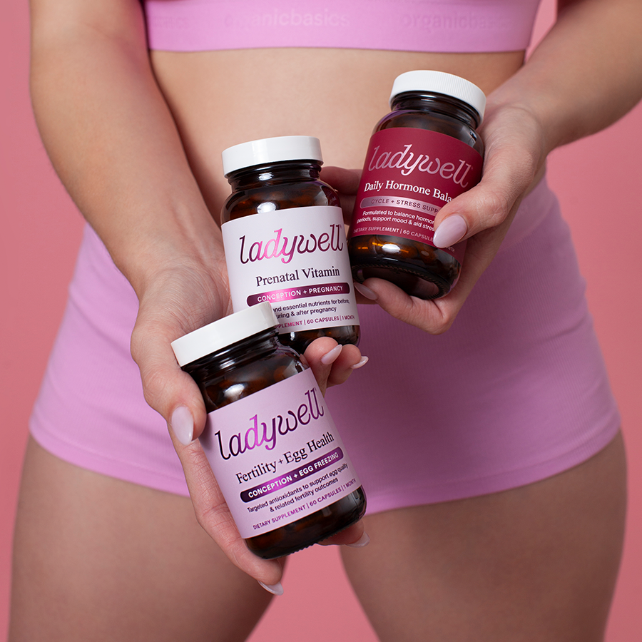 Three bottles of Ladywell supplements held by a person against a pink background