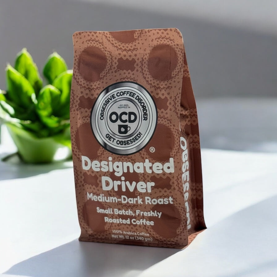 Coffee bag labeled 'Designated Driver' by OCD Coffee on a light surface with a plant in the background.