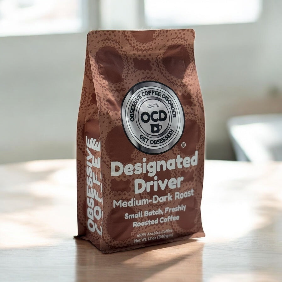 Coffee bag labeled 'Designated Driver' by OCD Coffee on a wooden surface with a blurred background.