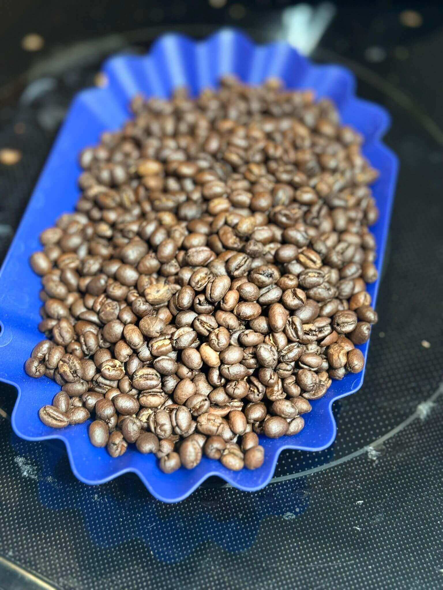 Roasted coffee beans in a blue silicone mold on a dark surface