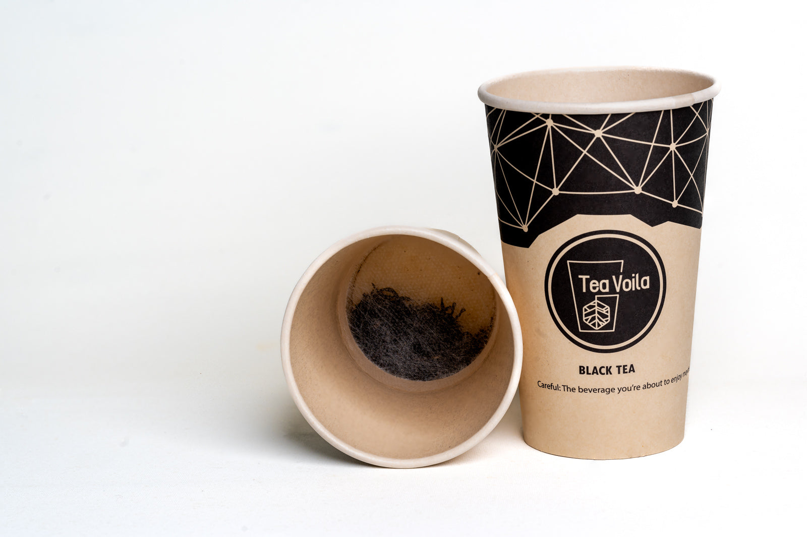 Two paper cups, one open showing black tea leaves, the other closed with 'Tea Voila' branding on a white background.